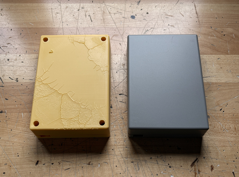 Two 3D printed enclosure parts side by side after 12 months of outdoor exposure showing yellowing on the ABS sample versus color stability on the ASA sample
