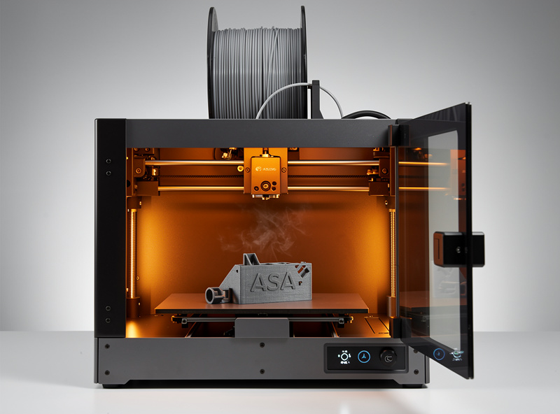 Enclosed 3D printer with chamber heated to printing temperature visible through the front door printing an ASA enclosure part