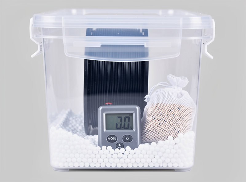 Sterilite gasket sealed cereal container converted to a 3D printer filament dry storage box with one filament spool inside silica gel desiccant packets and a small hygrometer reading 22 percent humidity