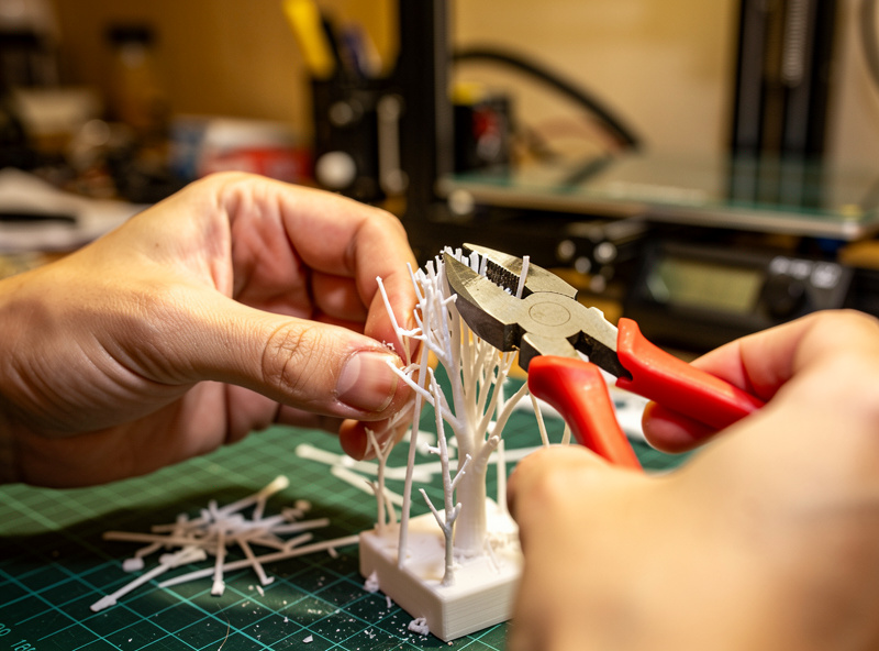 Person removing tree supports from a 3D printed model with side cutters