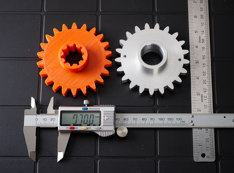 3D printed PLA prototype gear next to the same gear machined in aluminum on a black tile background