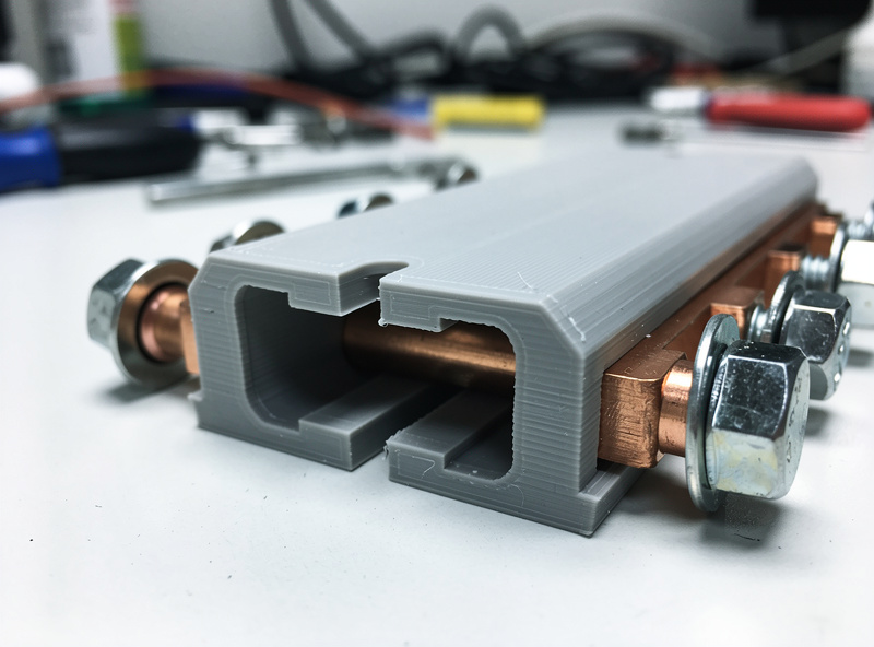 3D-printed U-channel bus bar cover clipped over nickel-plated copper bus bars between LiFePO4 terminals