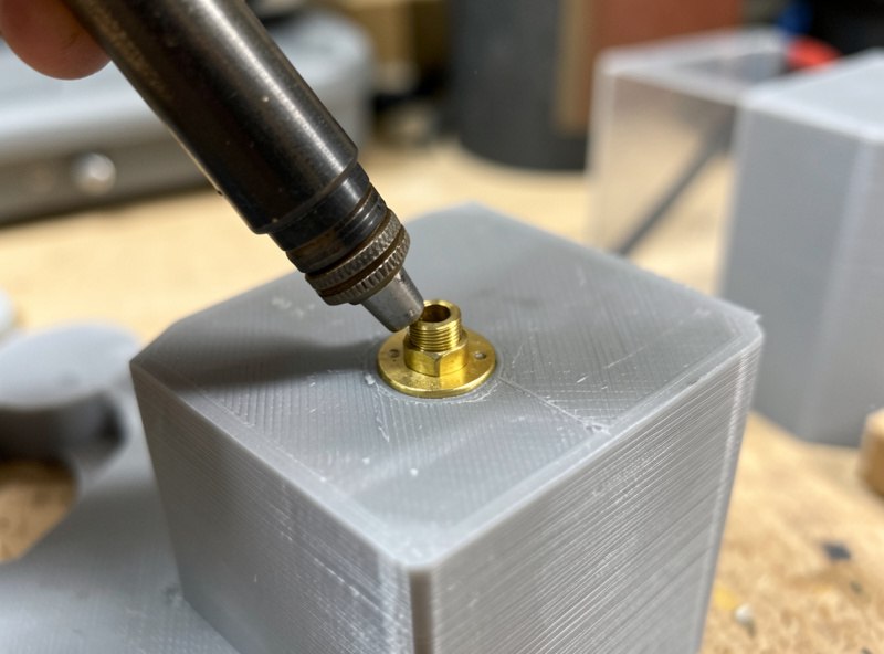 A soldering iron seating a brass heat-set insert into a 3D printed PETG part