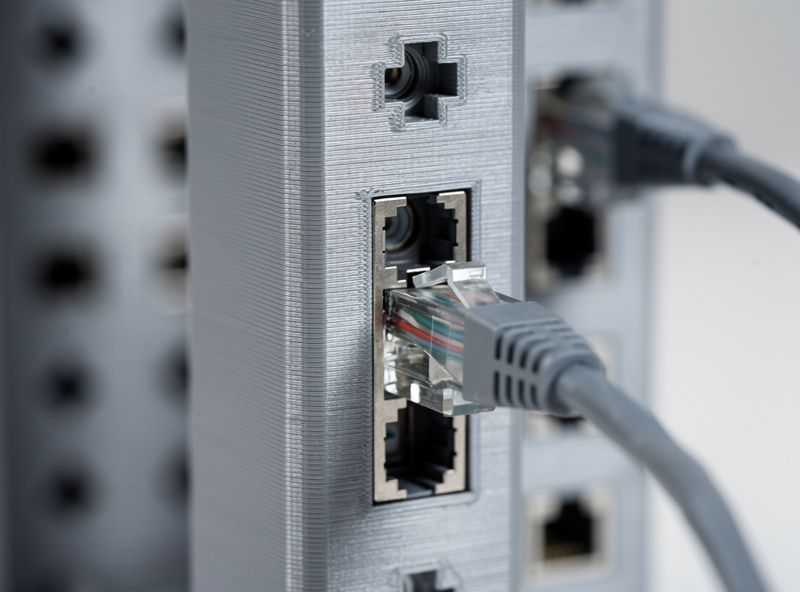 3D-printed PETG keystone panel installed in a network rack, Ethernet cables plugged into RJ45 keystone jacks, clean organized cable management, homelab setup